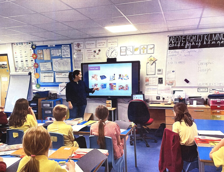 Ana is standing in front of a screen pointing at images of packing in front of a class of kids